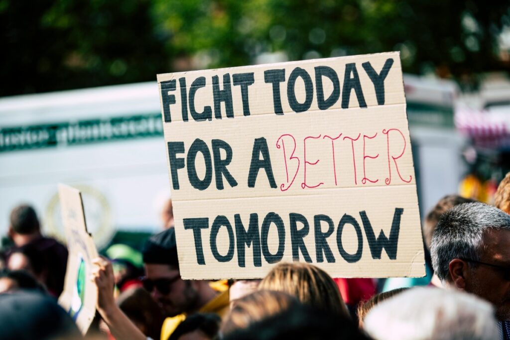 एक जनसमूह में से, एक कार्डबोर्ड का सिग्नल दिखाया जा रहा है, जिस पर "FIGHT TODAY FOR A BETTER TOMORROW" लिखा है। यह सिग्नल सुधार की渴求是 दर्शाता है। 2025 में भारत में सोशल मीडिया मार्केटिंग का परिदृश्य: इस तरह के सकारात्मक संदेशों का उपयोग सोशल मीडिया मार्केटिंग में किया जा सकता है, ताकि लोगों को प्रेरित किया जा सके और उनसे जुड़ाव स्थापित किया जा सके।