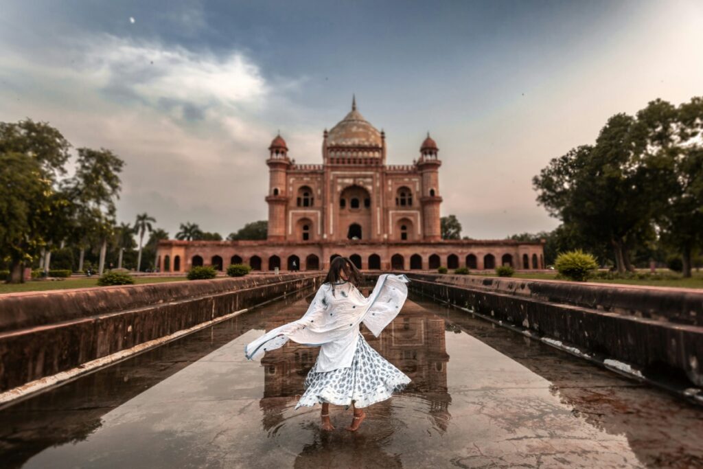 यह चित्र एक पुराने मकबरे जैसी सुंदर इमारत को दर्शाता है, जिसमें लाल पत्थर का इस्तेमाल किया गया है। इमारत के सामने एक महिला है, जो अपने कपड़े को हिलाती हुई पानी में खड़ी है। MX TakaTak पर अपने प्रोडक्ट को प्रमोट करने की रणनीति के समान, इस चित्र में भी आकर्षण का प्रयोग किया गया है। प्रोडक्ट प्रमोशन के लिए, आपको समान रूप से आकर्षक और दिलचस्प सामग्री बनानी होगी, जो दर्शकों का ध्यान आकर्षित करे।
