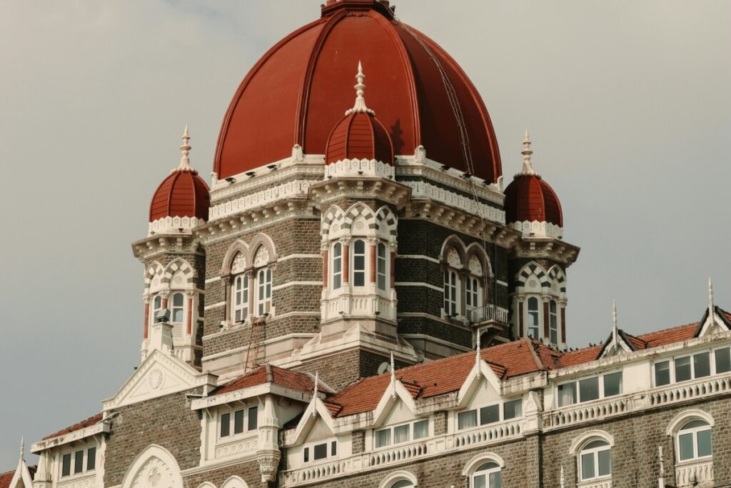 यह चित्र एक सुंदर ऐतिहासिक इमारत को दर्शाता है, जिसमें बड़ा लाल गुंबद और उसके चारों ओर छोटे - छोटे गुंबद हैं। इमारत में पुरानी - दिलचस्प वास्तुकला के तत्व भी दिखाई देते हैं। जिस प्रकार यह इमारत अपनी अनूठी सुंदरता और विशेषताओं से लोगों का ध्यान आकर्षित करती है, उसी प्रकार Moj पर अपने ब्रांड को पॉपुलर बनाने के लिए, आपको अपने ब्रांड की अनूठी पहचान बनानी होगी। आकर्षक सामग्री बनाएं, ट्रेंडिंग कंटेंट का प्रयोग करें, अपने दर्शकों के साथ सक्रिय रूप से जुड़ें और विशेष ऑफ़र या कैंपेन का आयोजन करें।